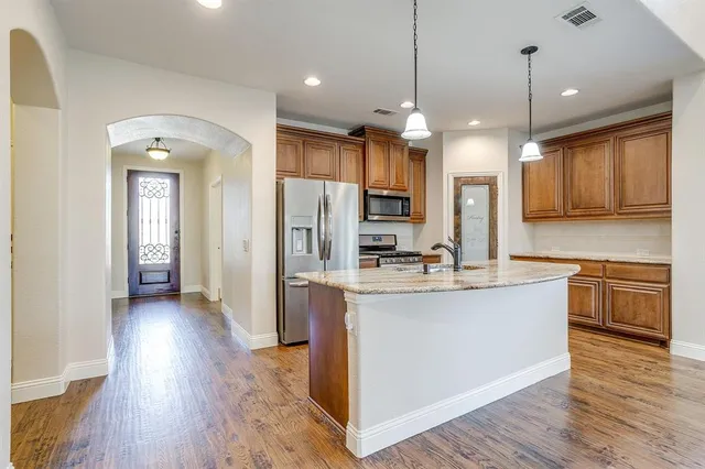 a kitchen with stainless steel appliances granite countertop a refrigerator a sink dishwasher a kitchen island with wooden floor and cabinets