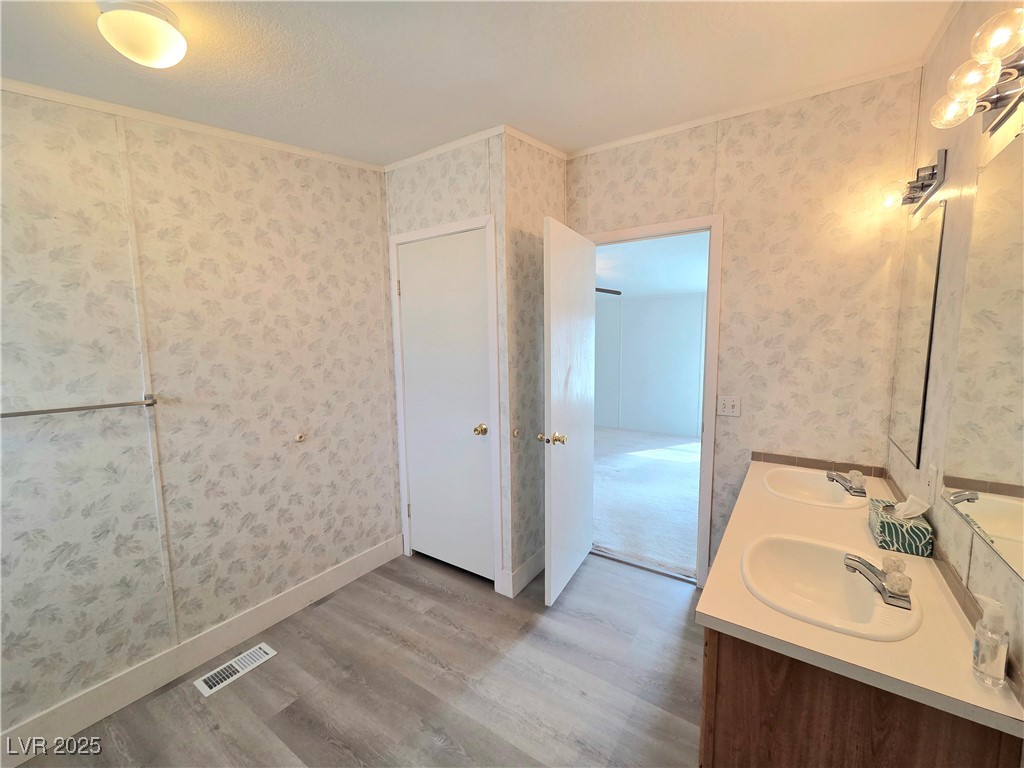 3290 Medicine Man Road Pahrump, NV 89048 - Photo 17 of 27 Full bathroom with light wood-style floors, double vanity, wallpapered walls, and crown molding