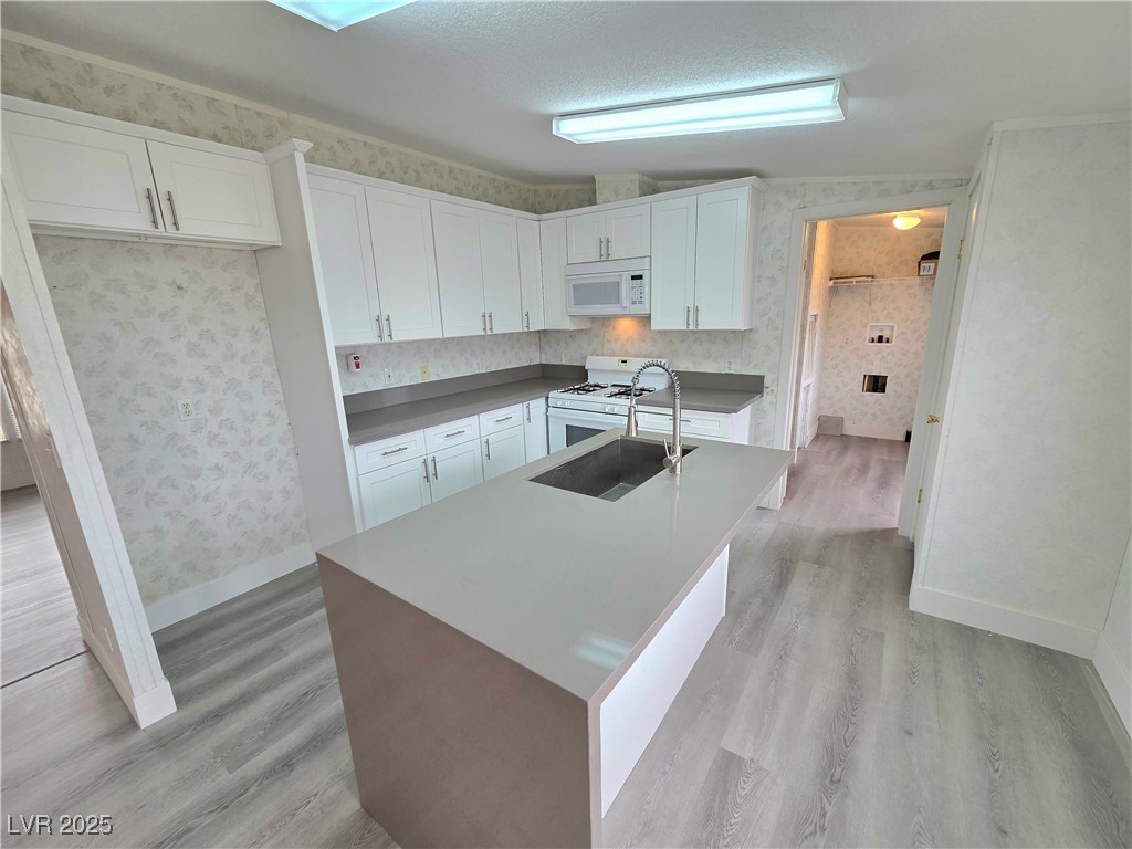 3290 Medicine Man Road Pahrump, NV 89048 - Photo 8 of 27 Kitchen with light wood-type flooring, white cabinets, white appliances, wallpapered walls, and a center island with sink