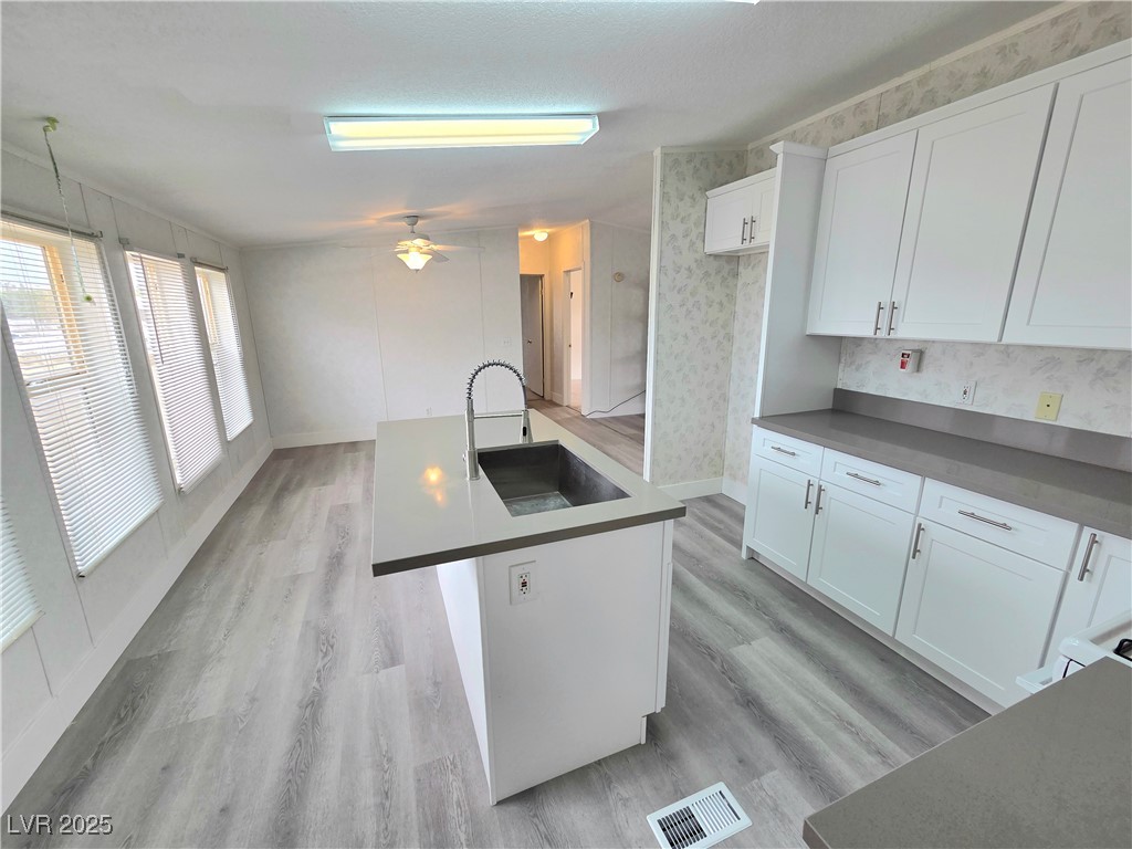 3290 Medicine Man Road Pahrump, NV 89048 - Photo 9 of 27 Kitchen with white cabinetry, an island with sink, light wood finished floors, and dark countertops