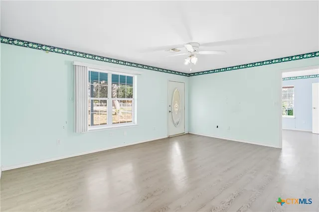 a view of an empty room with chandelier fan and wooden floor