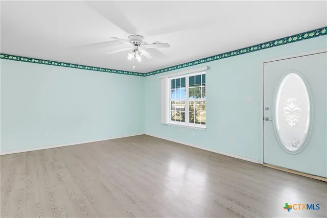 an empty room with wooden floor fan and windows