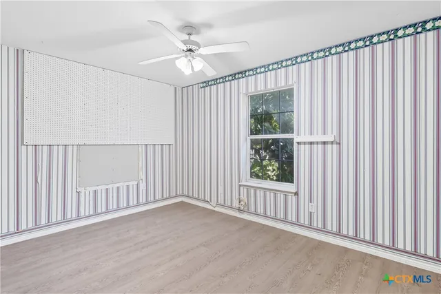 an empty room with wooden floor fan and windows