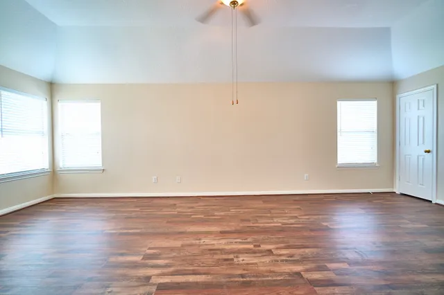 an empty room with wooden floor fan and windows