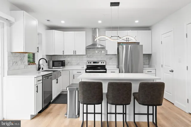 a kitchen with stainless steel appliances granite countertop a refrigerator a sink dishwasher a stove and white cabinets with wooden floor