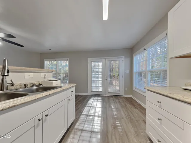 a open kitchen with granite countertop a stove a sink and white cabinets with wooden floor