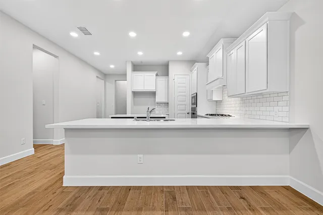 a large white kitchen with kitchen island a sink wooden floor and stainless steel appliances
