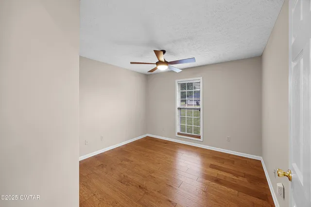 an empty room with wooden floor ceiling fan and windows