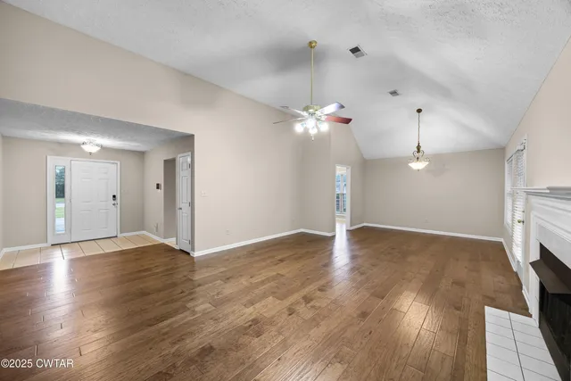 a view of an empty room with wooden floor and a ceiling fan