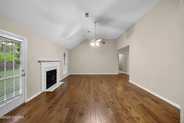 an empty room with wooden floor fireplace and windows