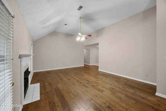 a view of an empty room with wooden floor and a ceiling fan