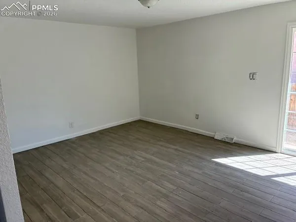 a view of an empty room with wooden floor and a window