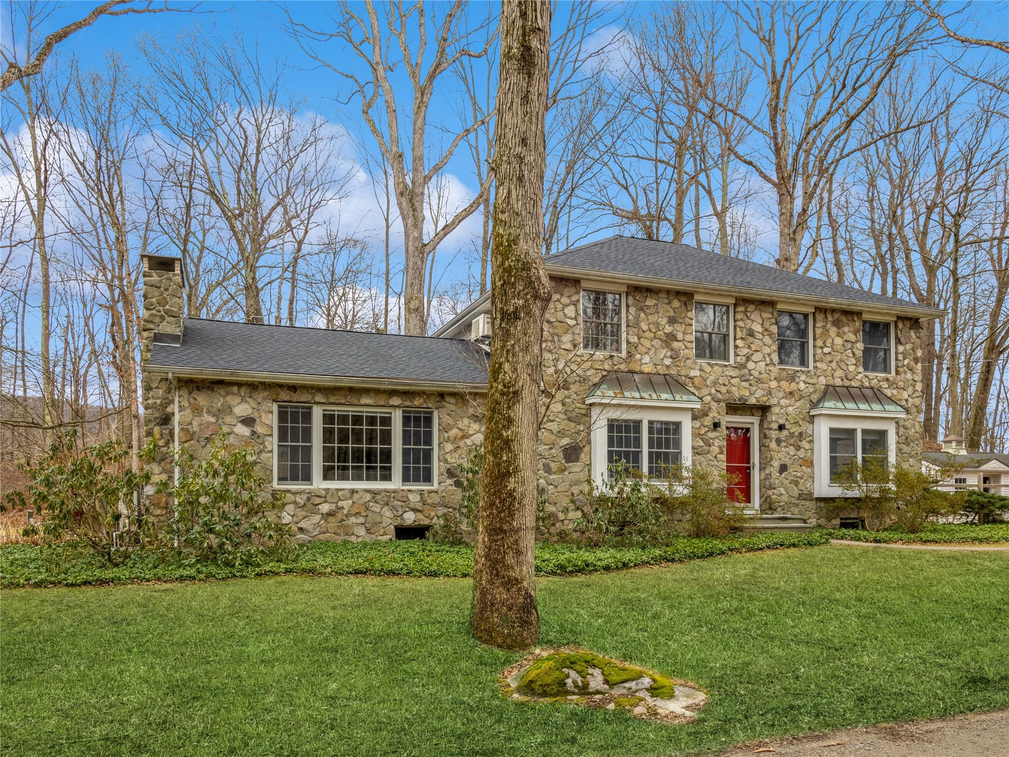 Colonial inspired home featuring stone siding,a front yard, and roof with shingles