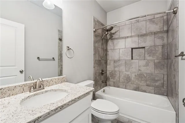 a bathroom with a granite countertop bathtub shower sink vanity mirror and toilet