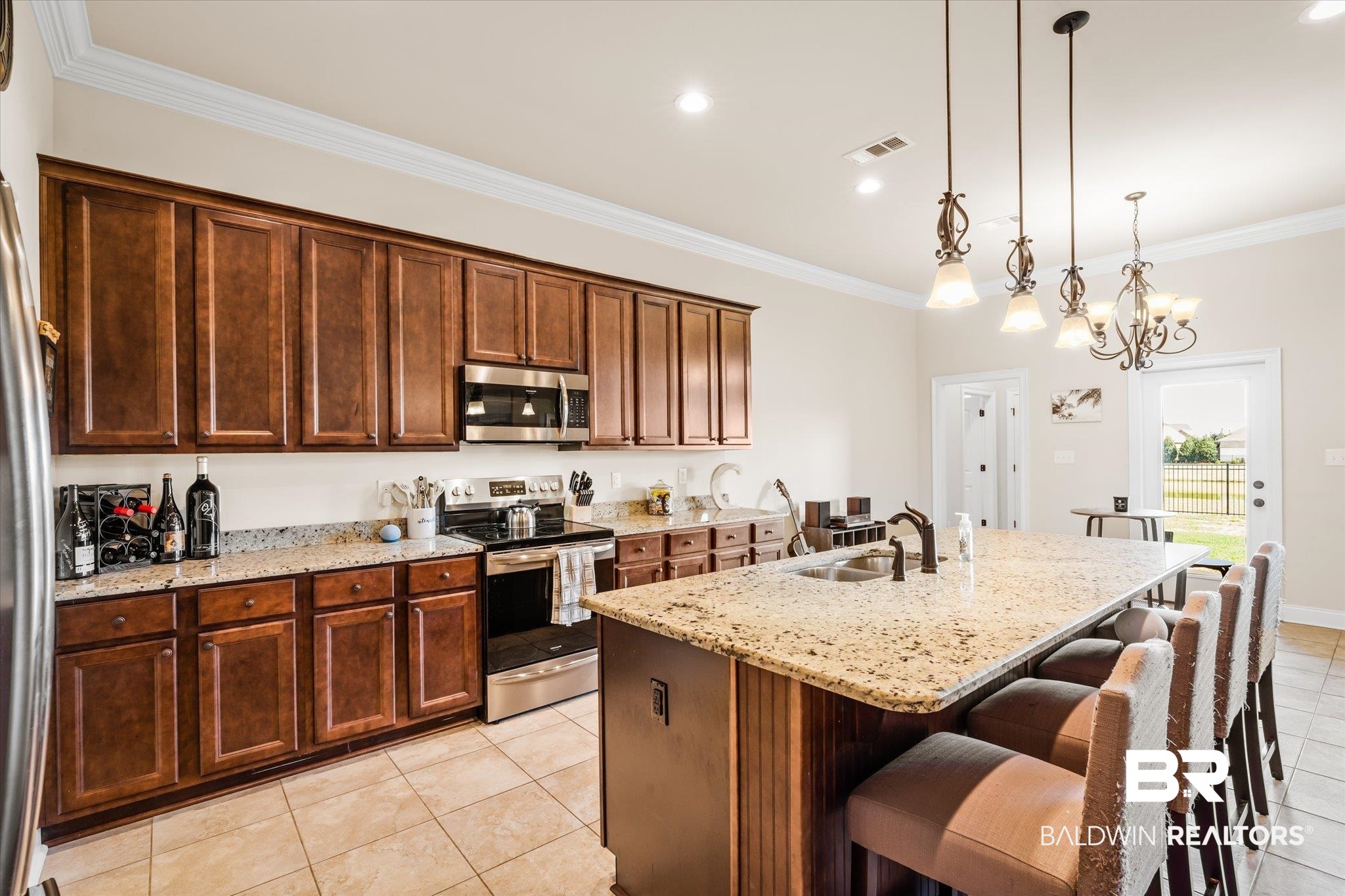 Kitchen featuring appliances with stainless steel finishes, light stone countertops, decorative light fixtures, a breakfast bar area, and an island with sink