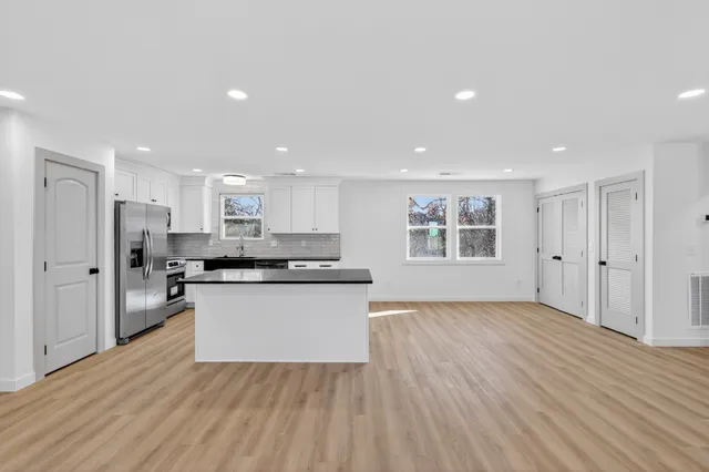 a open kitchen with kitchen island a sink dishwasher a refrigerator and white cabinets with wooden floor