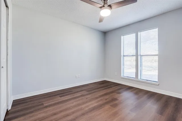 an empty room with wooden floor fan and windows