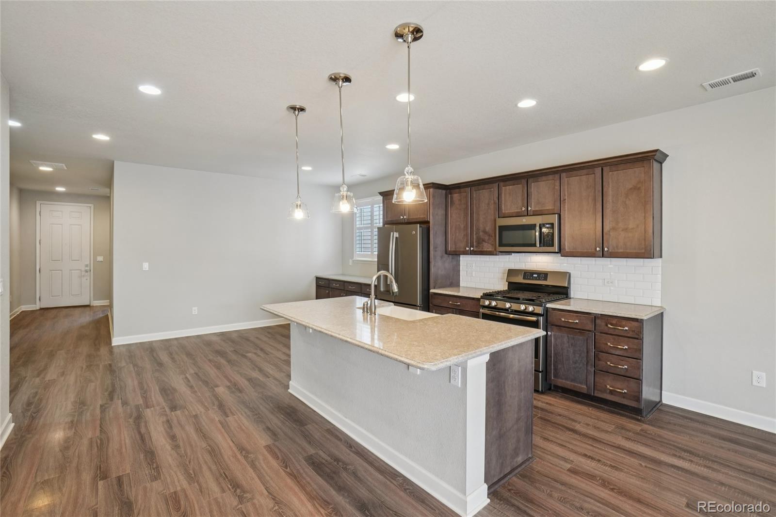 6523 Independence Street Frederick, CO 80516 - Photo 6 of 21 a large kitchen with stainless steel appliances granite countertop a stove a sink a refrigerator and a microwave oven with wooden floor