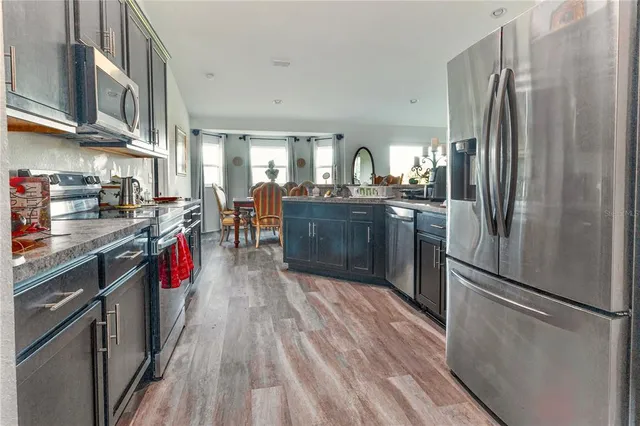 a kitchen with stainless steel appliances granite countertop a refrigerator a stove top oven a sink dishwasher and wooden cabinets with wooden floor