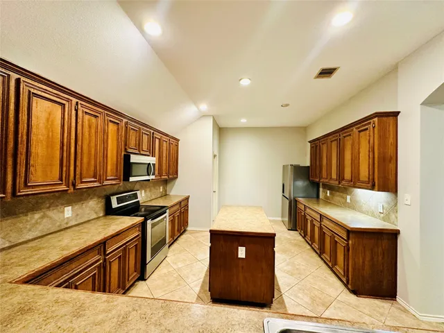 a large kitchen with stainless steel appliances wooden cabinets a stove and a sink