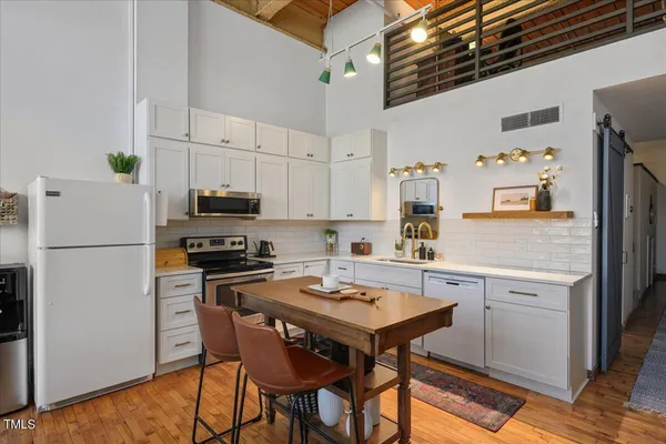 a kitchen with stainless steel appliances a stove a sink refrigerator and white cabinets with wooden floor