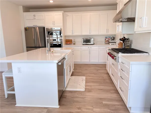 a kitchen with stainless steel appliances a stove top oven a refrigerator a sink and dishwasher with wooden floor