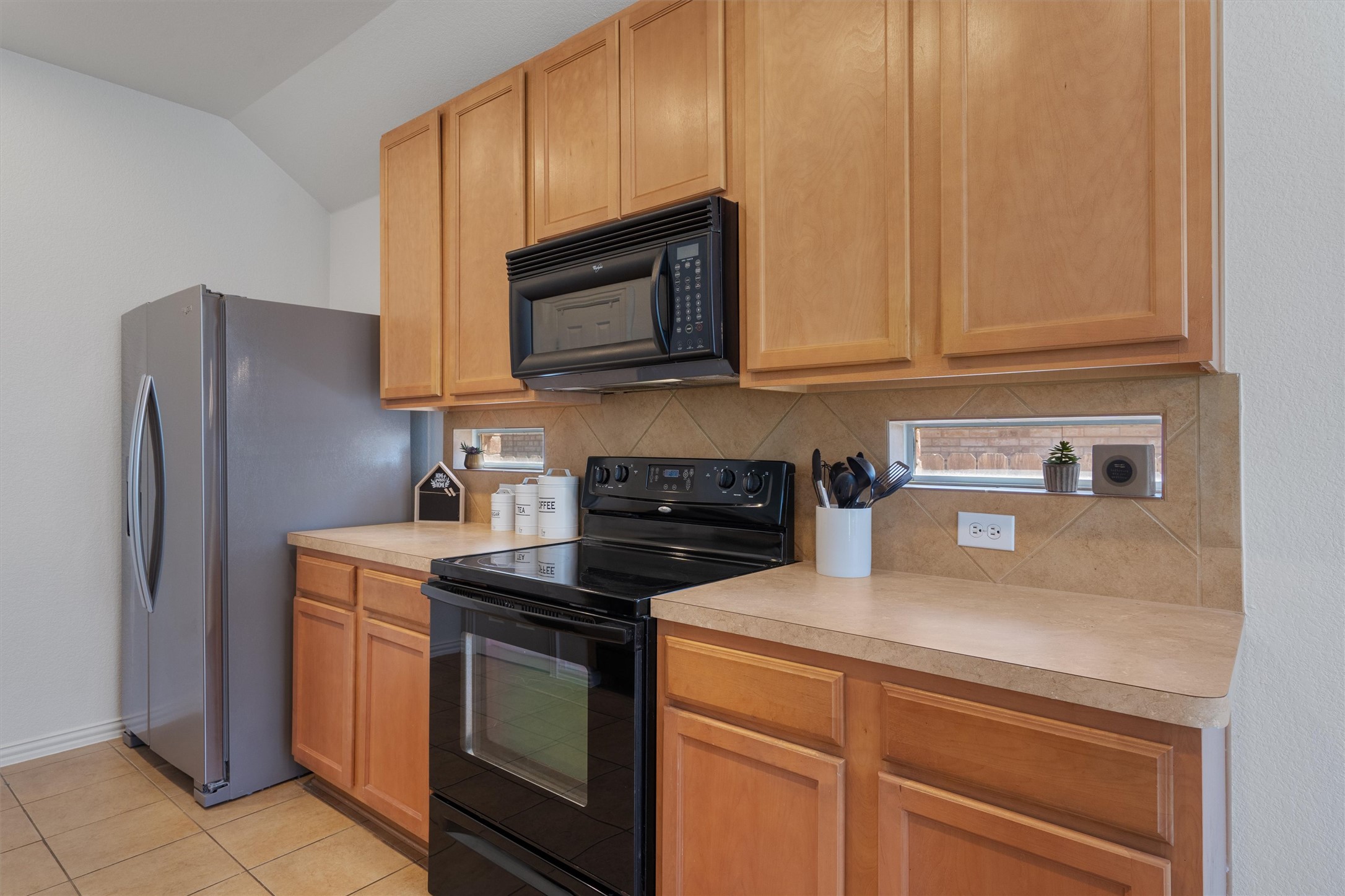 2801 Kickapoo Cavern Drive Pflugerville, TX 78660 - Photo 15 of 38 Kitchen with black appliances, light countertops, decorative backsplash, vaulted ceiling, and light tile patterned flooring