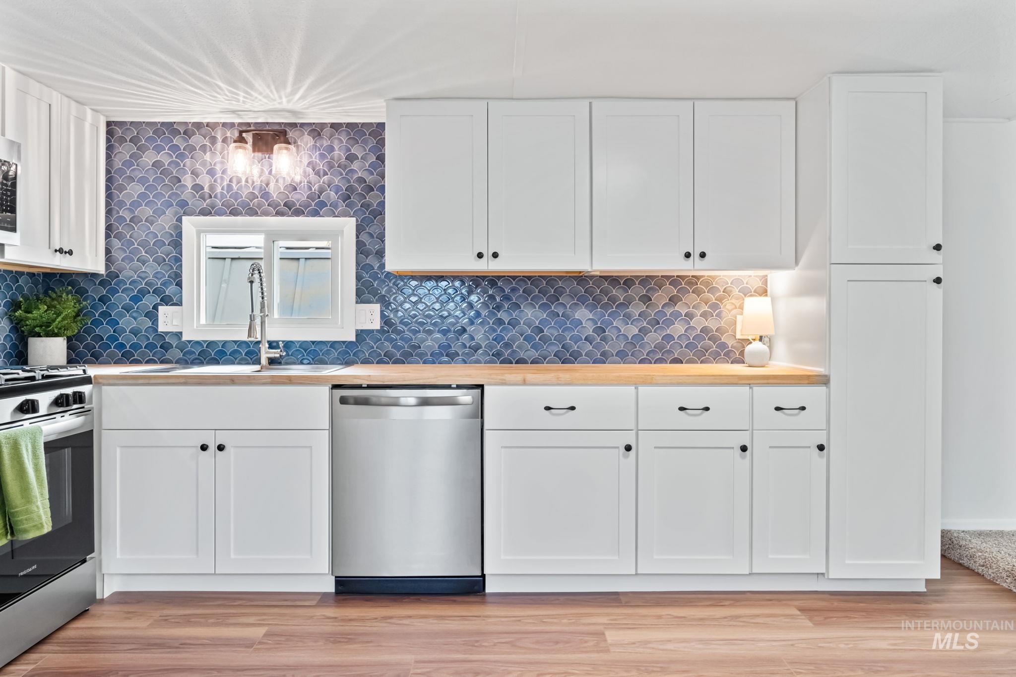 Kitchen featuring appliances with stainless steel finishes, white cabinetry, decorative backsplash, light wood-type flooring, and wooden counters