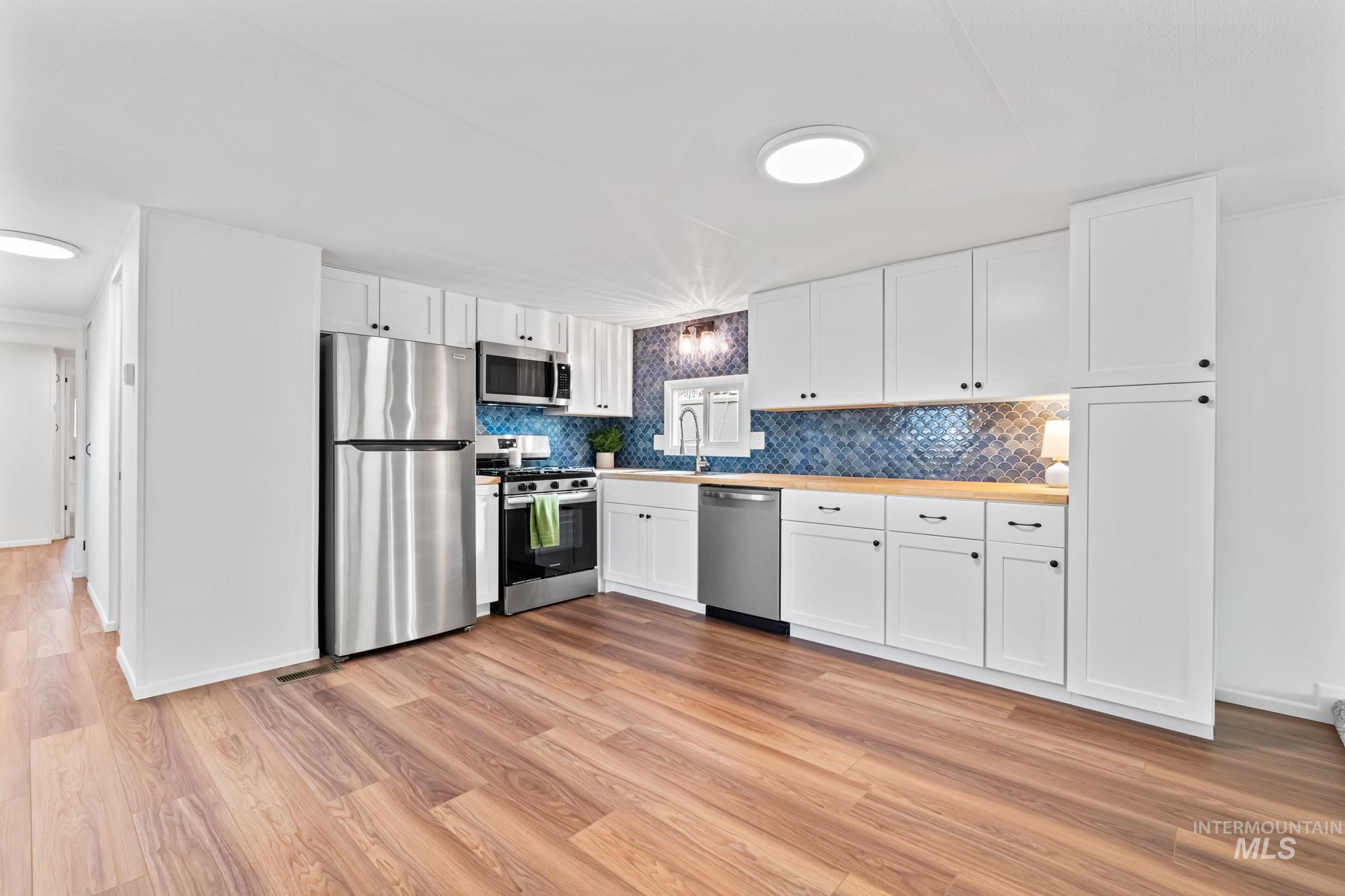358 Bonanza Street Boise, ID 83713 - Photo 7 of 25 Kitchen featuring white cabinetry, stainless steel appliances, light wood-style flooring, light countertops, and decorative backsplash