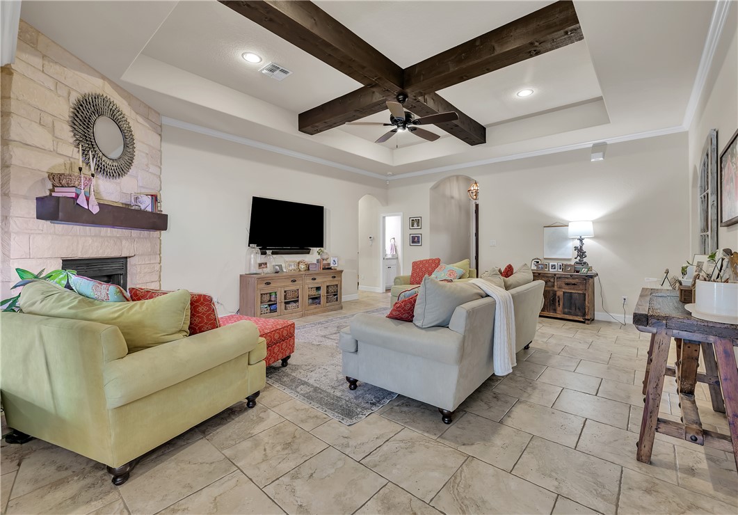 8312 Raintree Drive College Station, TX 77845 - Photo 5 of 30 Spacious living area featuring a coffered ceiling with exposed wood beams, a stone-faced fireplace with a wood mantel, light-toned tile flooring, and recessed lighting