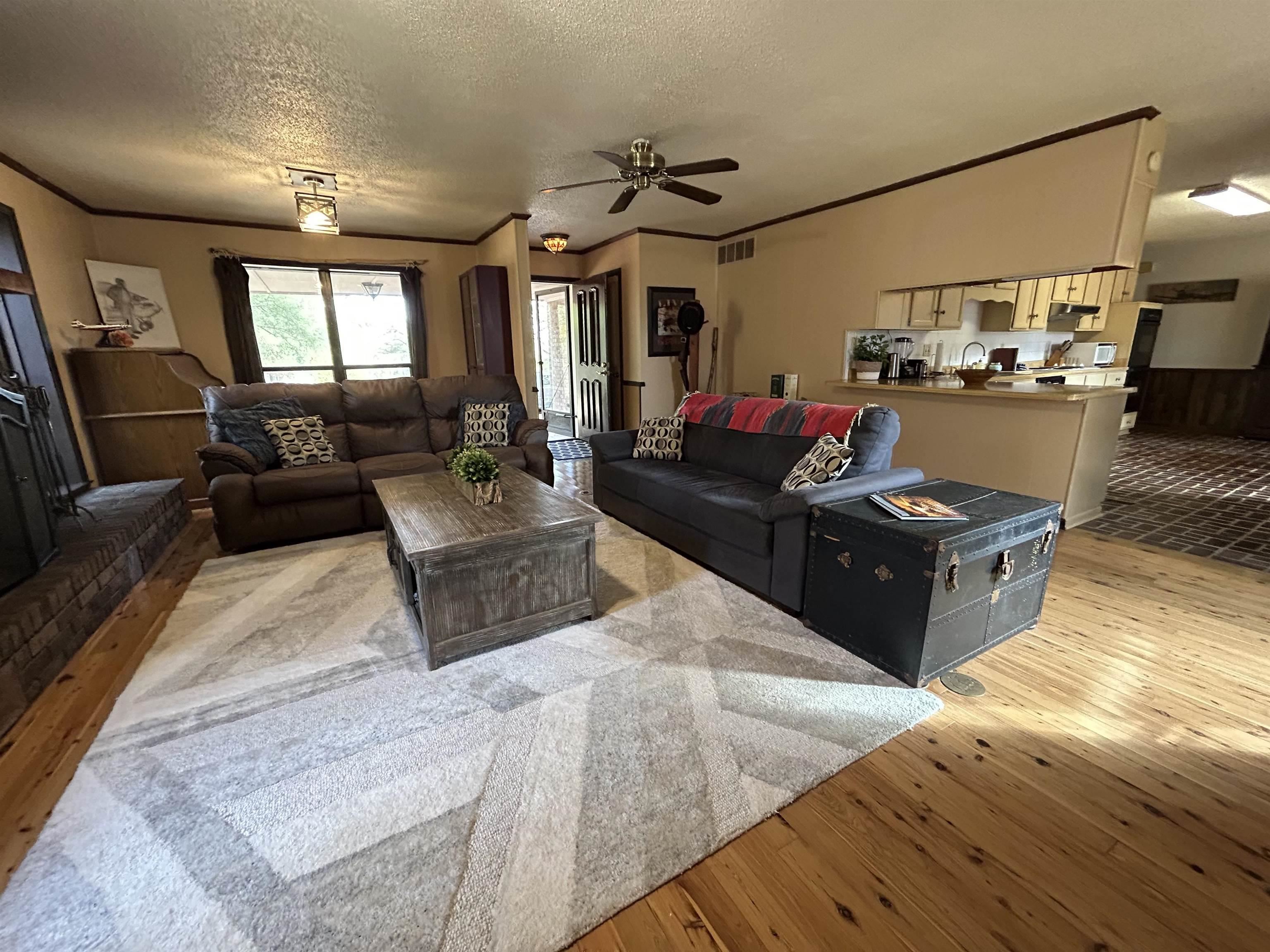 Living room featuring crown molding, light wood-style floors, a ceiling fan, and a textured ceiling