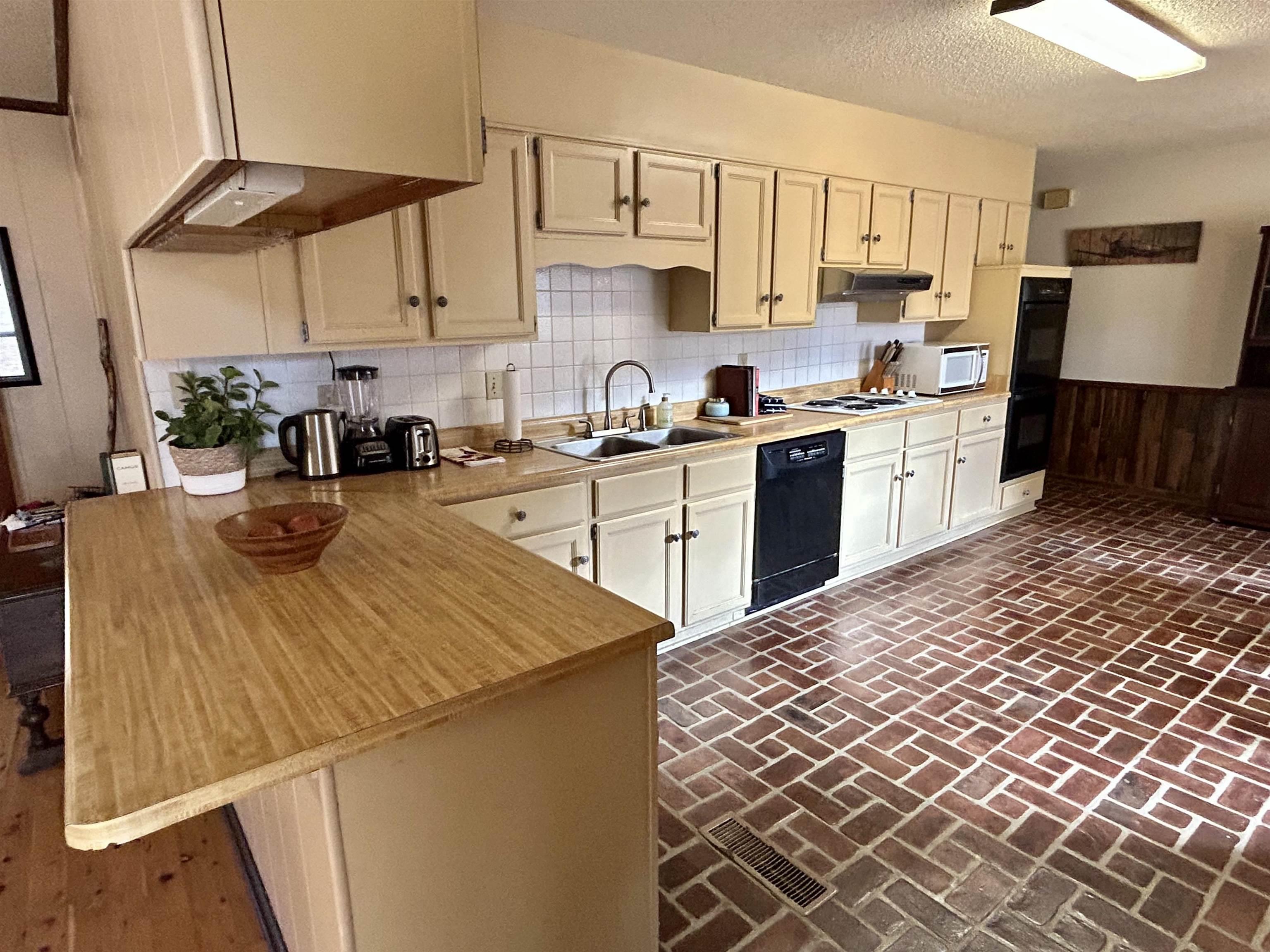 Kitchen featuring brick floors, light countertops, tasteful backsplash, black appliances, and a textured ceiling