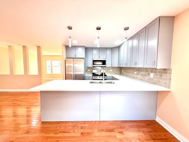 a kitchen with kitchen island granite countertop a sink a stove a refrigerator and white cabinets with wooden floor