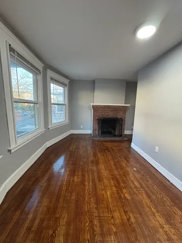 an empty room with wooden floor fireplace and windows
