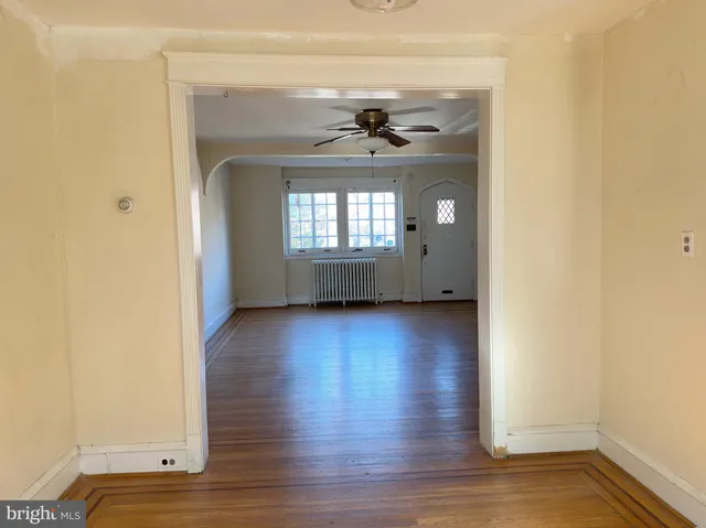 a view of a hallway to an empty room with wooden floor and a window