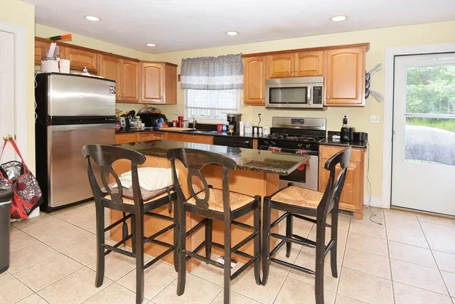 a kitchen with stainless steel appliances granite countertop a dining table chairs refrigerator and sink