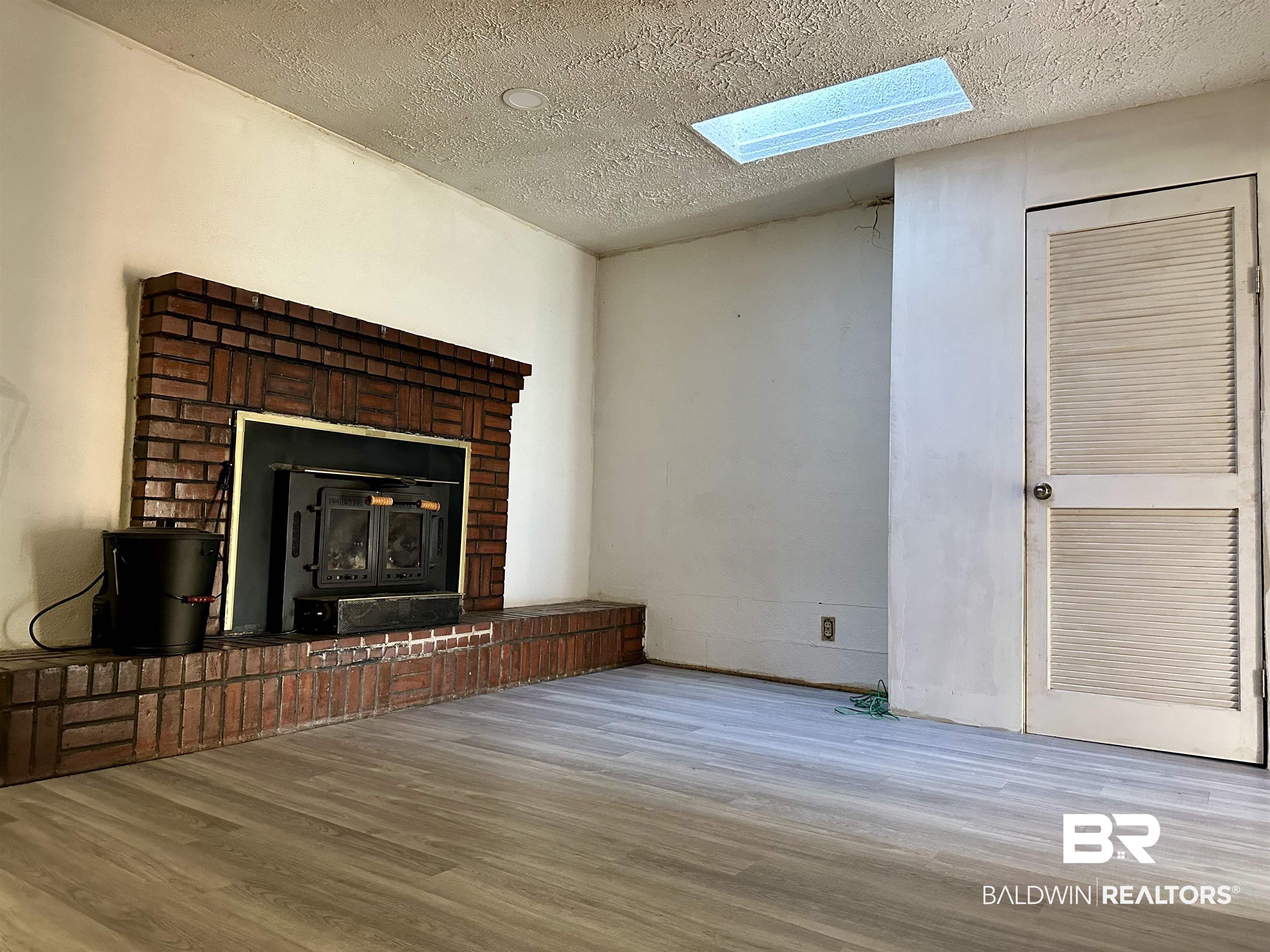 1206 St Nicholas Avenue Brewton, AL 36426 - Photo 4 of 19 Unfurnished living room featuring light hardwood / wood-style flooring, a textured ceiling, and a wood stove