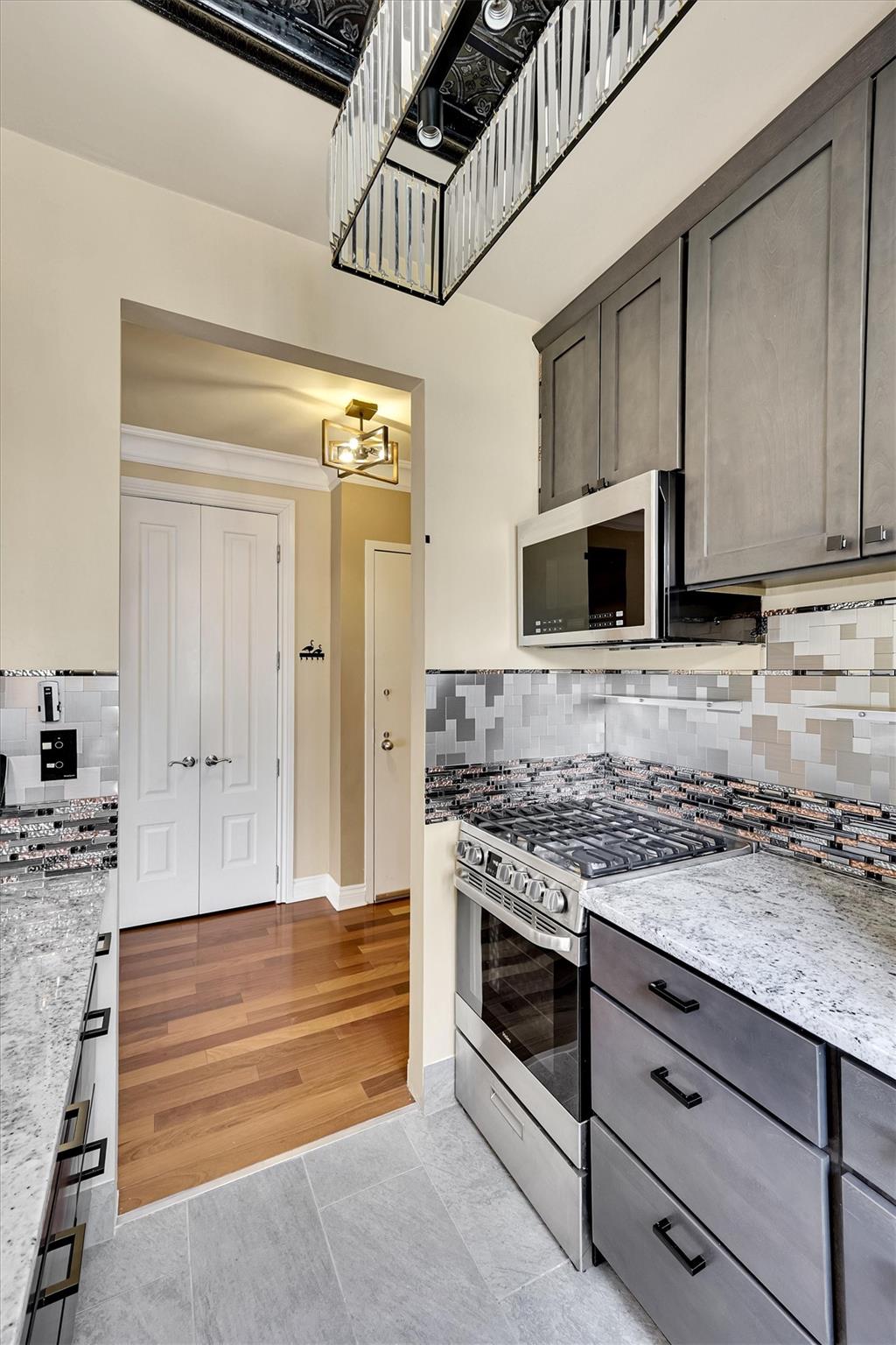 380 Rector Place, Unit 15E Manhattan, NY 10280 - Photo 11 of 31 Kitchen with light stone counters, backsplash, stainless steel appliances, an inviting chandelier, and light wood finished floors