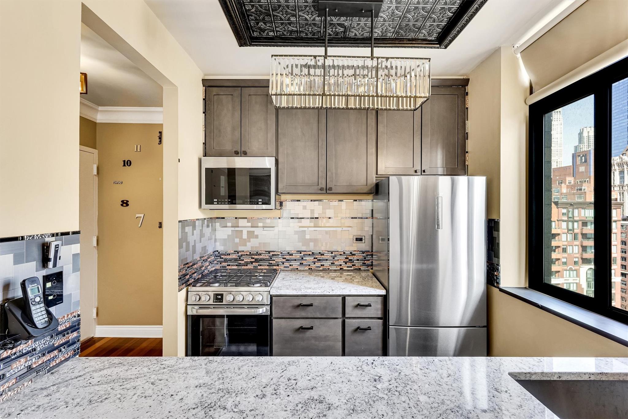 380 Rector Place, Unit 15E Manhattan, NY 10280 - Photo 12 of 31 Kitchen with tasteful backsplash, light stone countertops, dark brown cabinetry, a chandelier, and stainless steel appliances