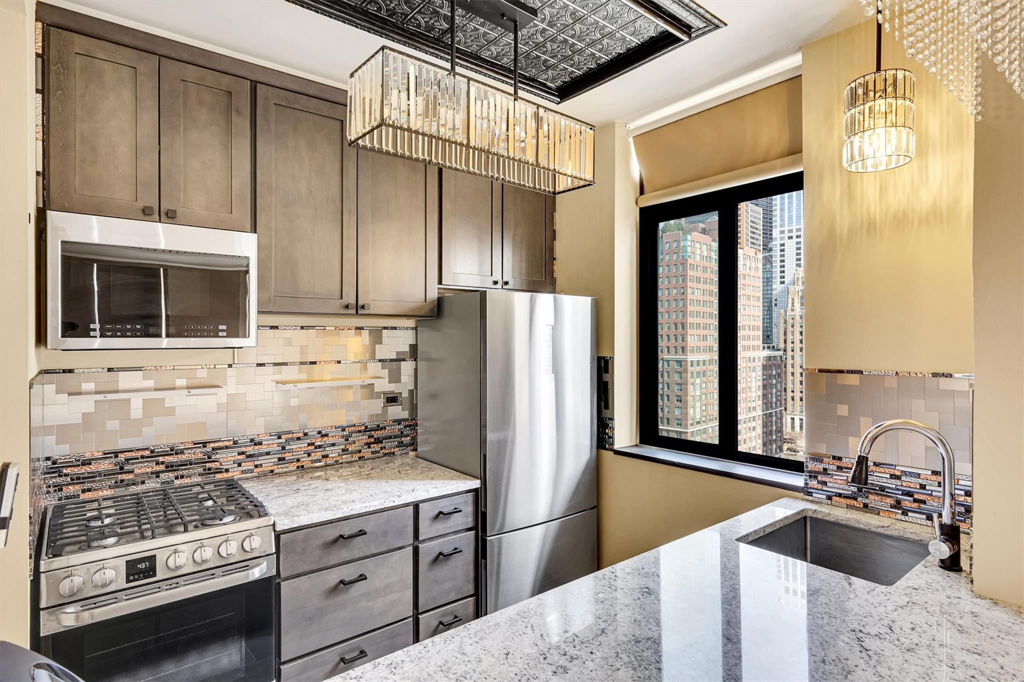 380 Rector Place, Unit 15E Manhattan, NY 10280 - Photo 13 of 31 Kitchen featuring backsplash, light stone counters, appliances with stainless steel finishes, an inviting chandelier, and a sink