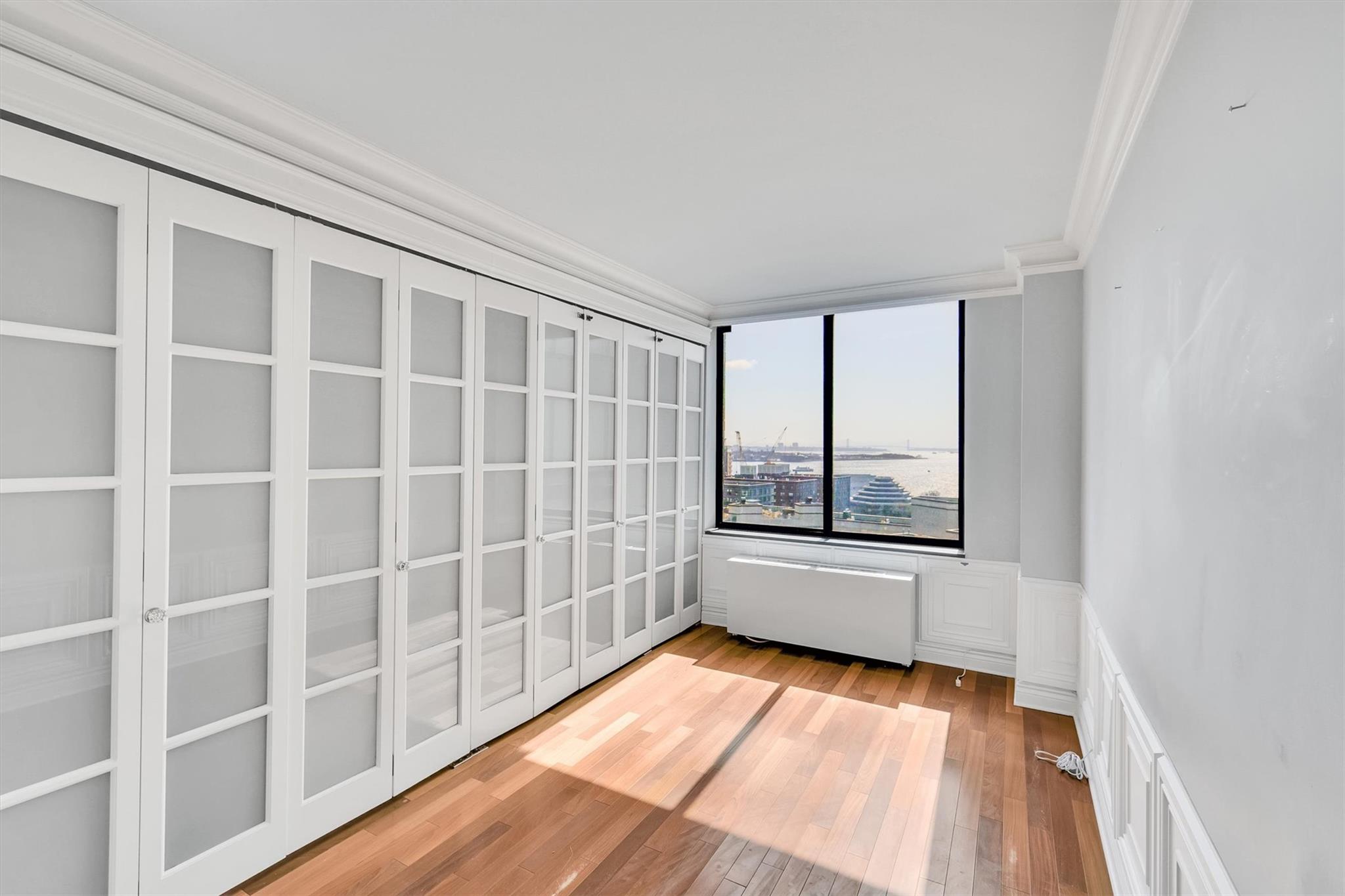 380 Rector Place, Unit 15E Manhattan, NY 10280 - Photo 22 of 31 Empty room featuring radiator, hardwood / wood-style flooring, wainscoting, crown molding, and a decorative wall