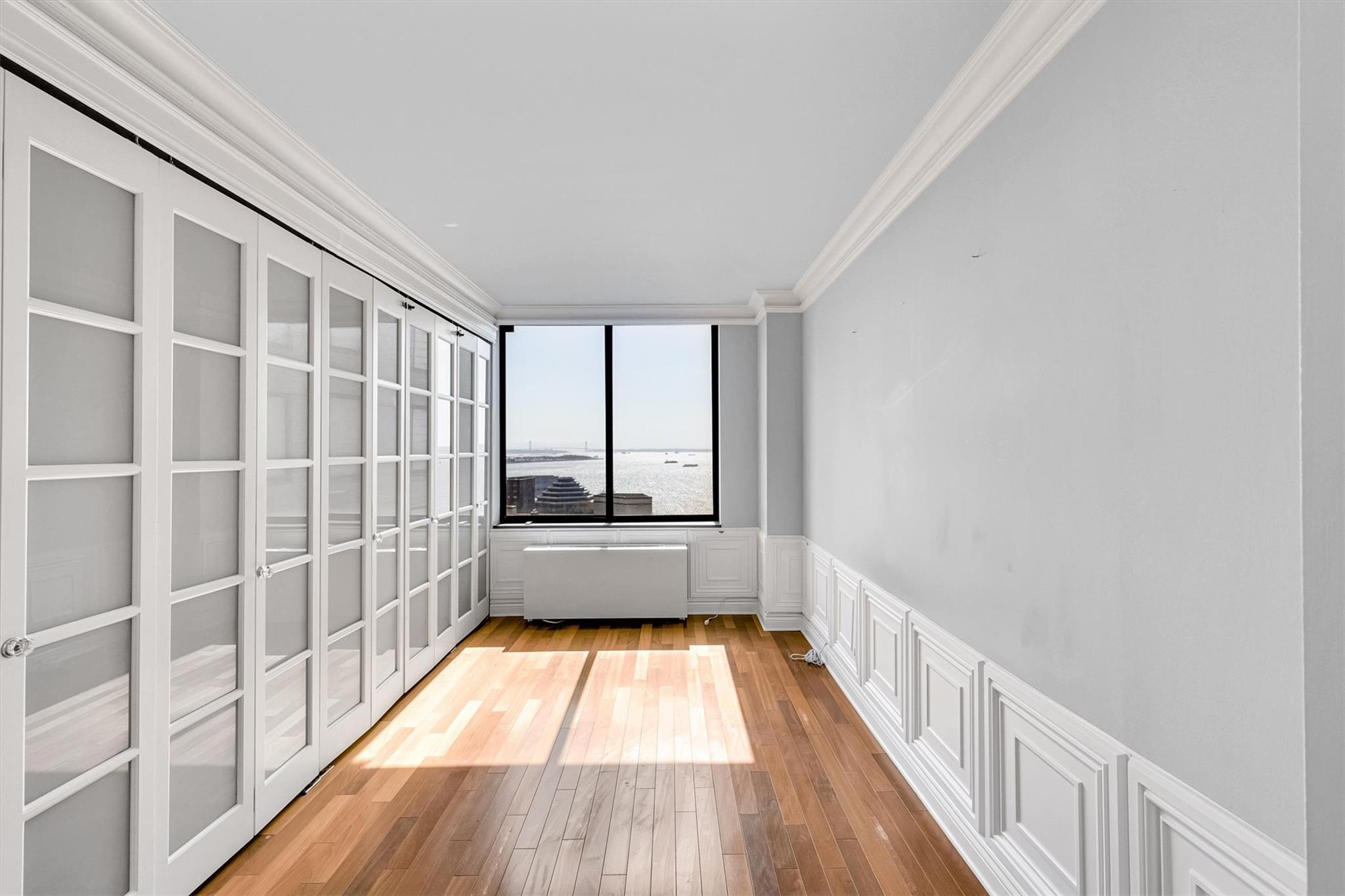 380 Rector Place, Unit 15E Manhattan, NY 10280 - Photo 24 of 31 Unfurnished room with a wainscoted wall, radiator heating unit, a decorative wall, crown molding, and light wood finished floors