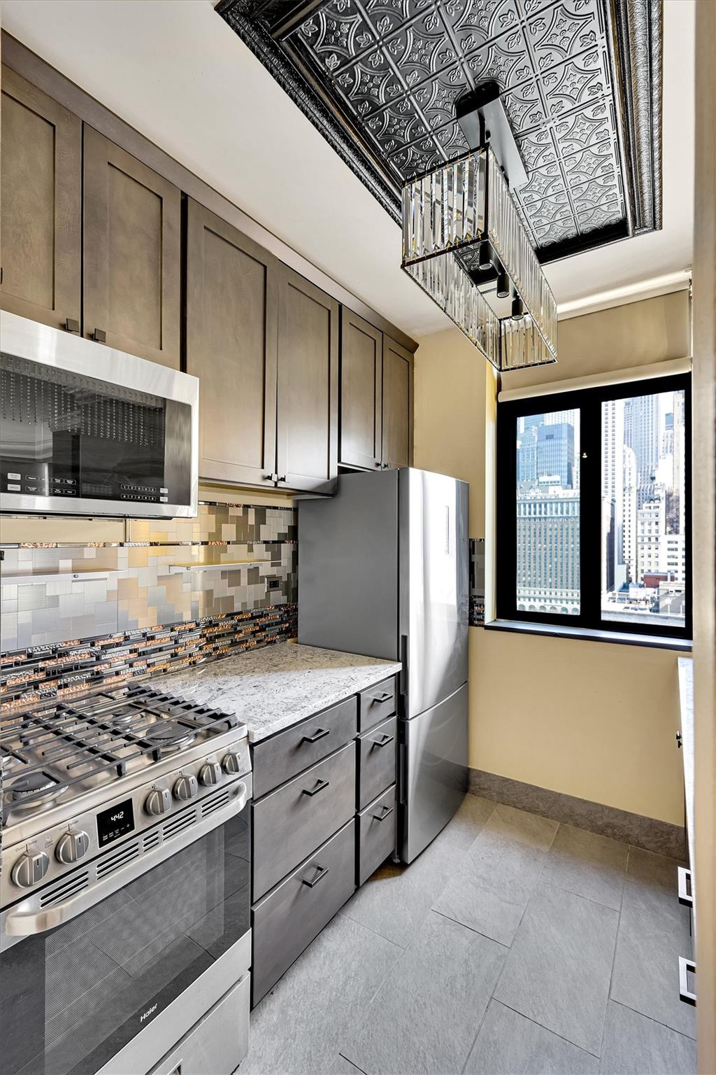 380 Rector Place, Unit 15E Manhattan, NY 10280 - Photo 9 of 31 Kitchen with light tile patterned floors, baseboards, dark brown cabinets, appliances with stainless steel finishes, and backsplash