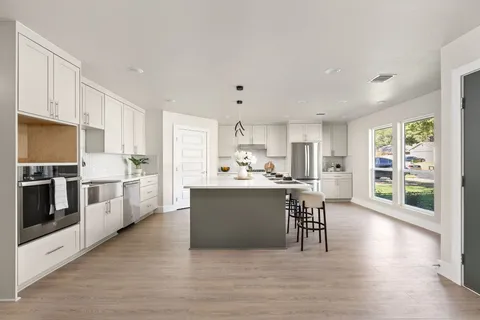 a kitchen with stainless steel appliances granite countertop a refrigerator a stove top oven a sink dishwasher and white cabinets with wooden floor