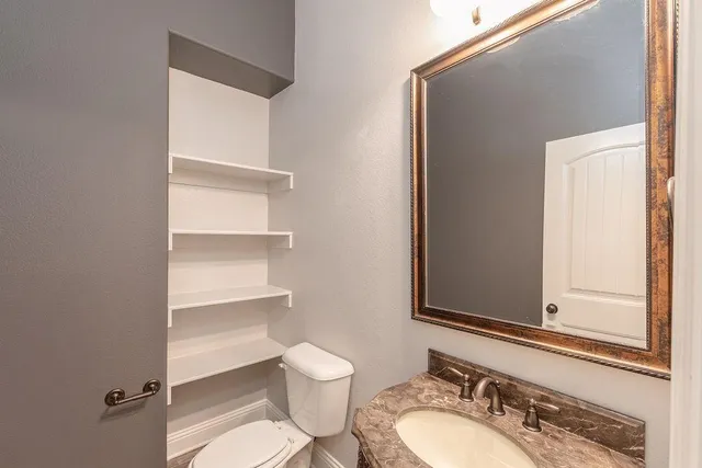 a bathroom with a granite countertop sink vanity mirror and toilet