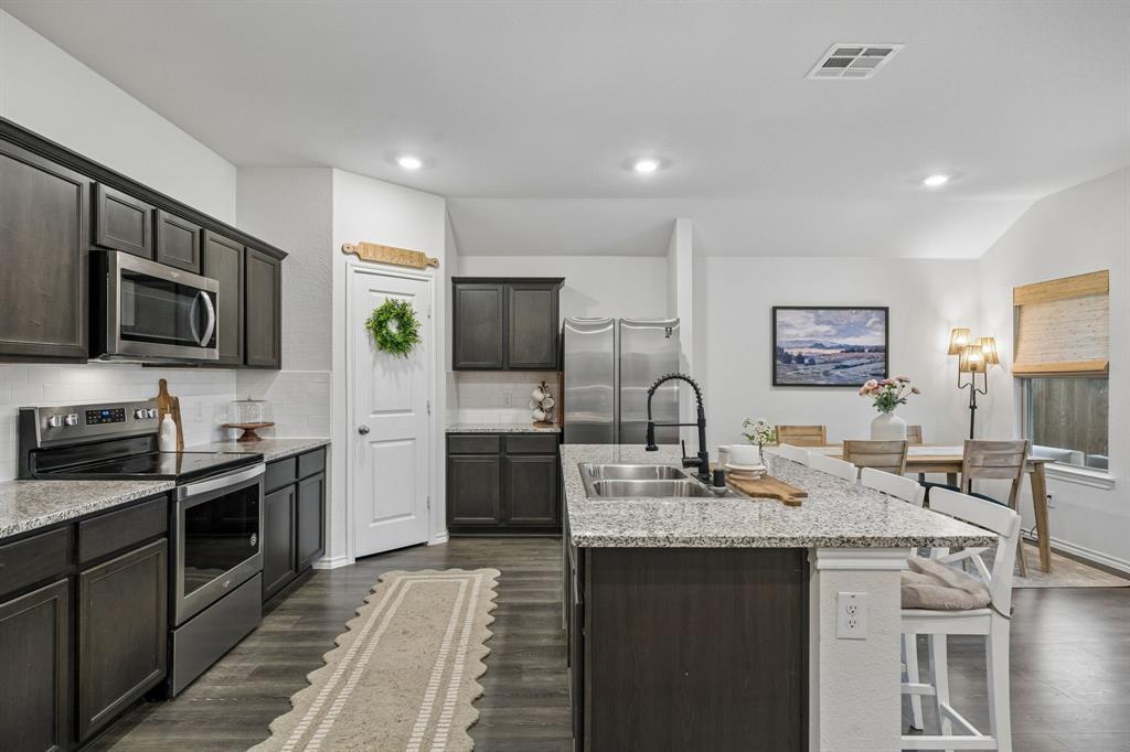 1107 Ringgold Road Forney, TX 75126 - Photo 14 of 27 Kitchen featuring dark wood-finish cabinetry, stainless steel appliances, granite countertops, and white subway tile backsplash