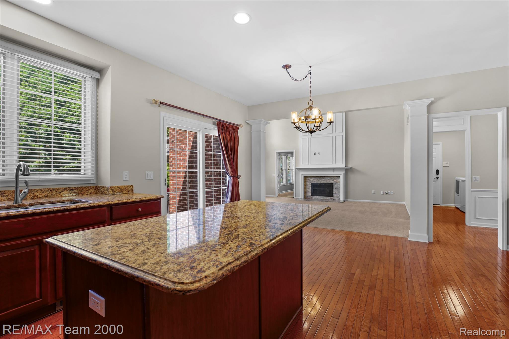 1248 Lasalle Road Canton, MI 48187 - Photo 35 of 67 Kitchen island with granite countertop and rich wood cabinetry, offering a view into a living area featuring a fireplace with stone surround and a decorative mantle
