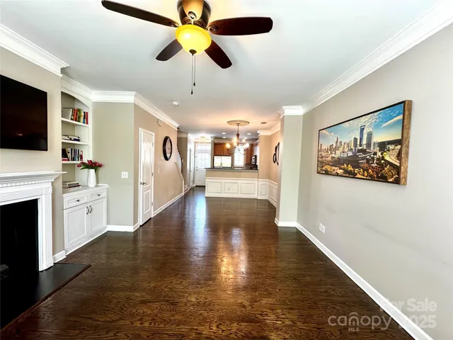 a view of a livingroom with wooden floor a ceiling fan and kitchen view