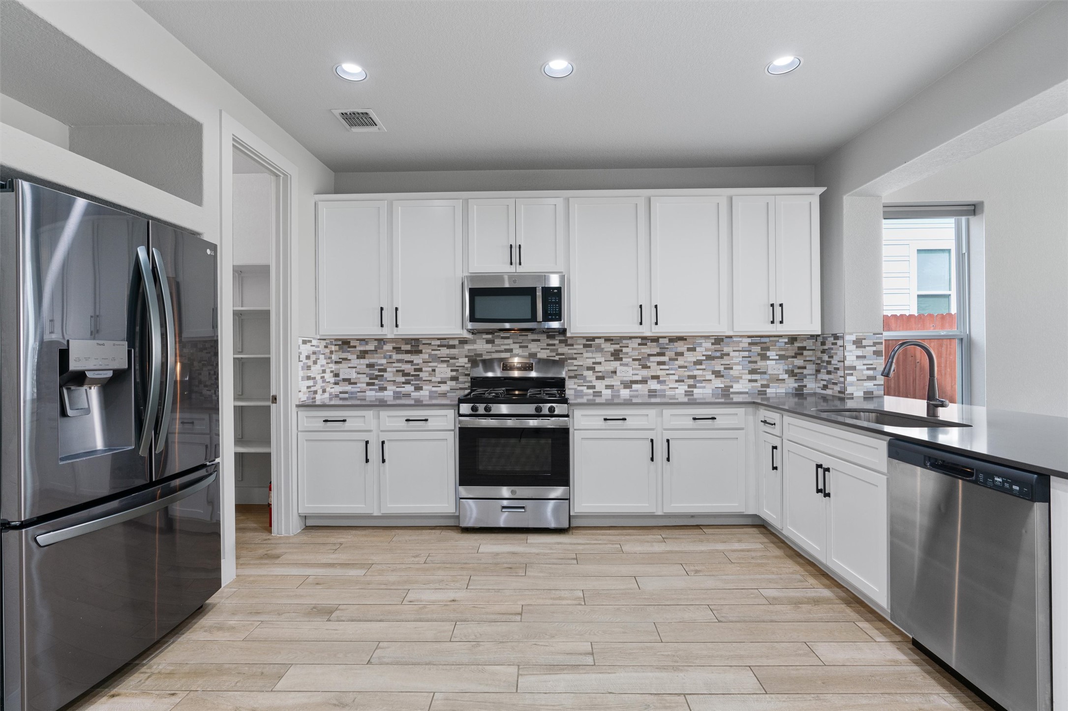 11217 Charger Way Manor, TX 78653 - Photo 5 of 35 Kitchen with stainless steel appliances, white cabinets, recessed lighting, light stone countertops, and light wood-style flooring