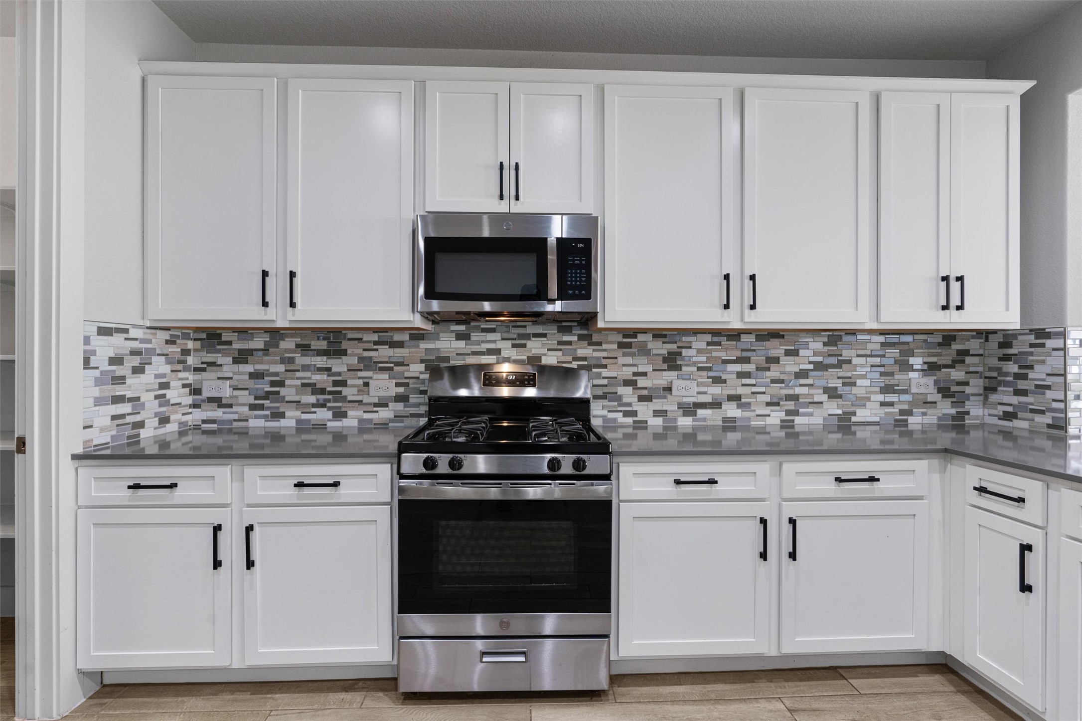 11217 Charger Way Manor, TX 78653 - Photo 6 of 35 Kitchen featuring stainless steel appliances, white cabinetry, backsplash, and light stone countertops